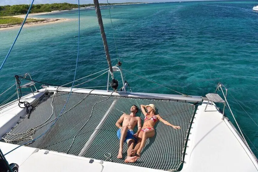 Couple lying on the net deck of a catamaran over clear water